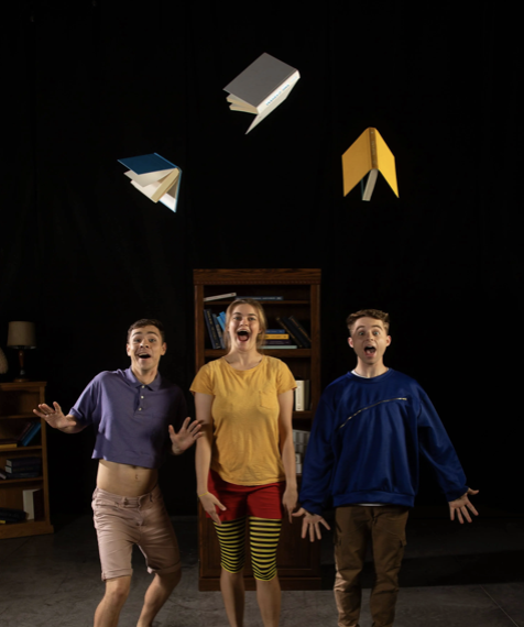 Three excited individuals joyfully react to floating books above them, set against a black background with a wooden bookshelf behind.